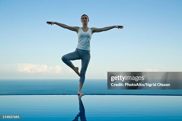 woman standing in tree pose on edge of infinity pool - standing on one leg stock-fotos und bilder