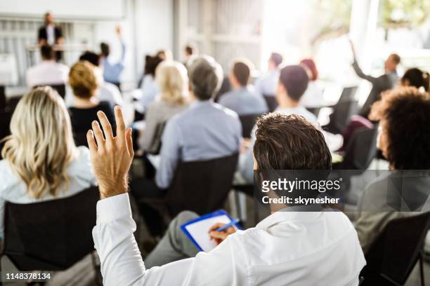 vista trasera de un empresario levantando la mano en un seminario. - finance talk fotografías e imágenes de stock