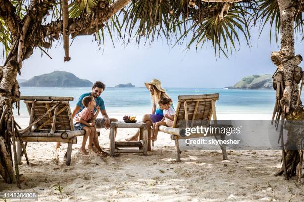 happy family talking while relaxing on deck chairs at the beach. - indonesia travel stock pictures, royalty-free photos & images