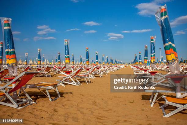 a line of beach umbrellas and lounge chairs on sand beach, bibione, veneto, italy - bibione stock pictures, royalty-free photos & images