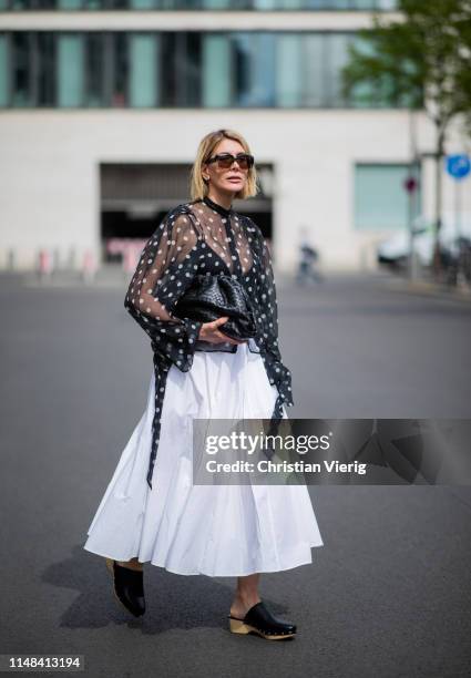 Victoria Nasir is seen wearing white pleated poplin a-line skirt COS, transparent blouse with polka dots Petar Petrov, clogs Zara, black the pouch...