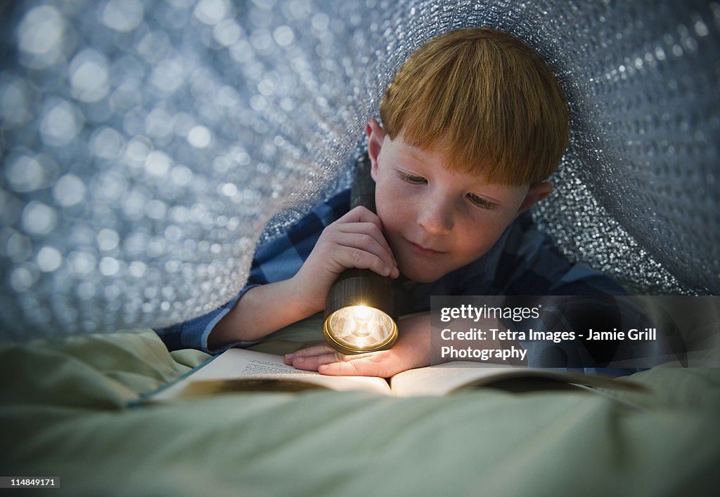 USA, New Jersey, Jersey City, Boy (8-9) reading book under bed covers