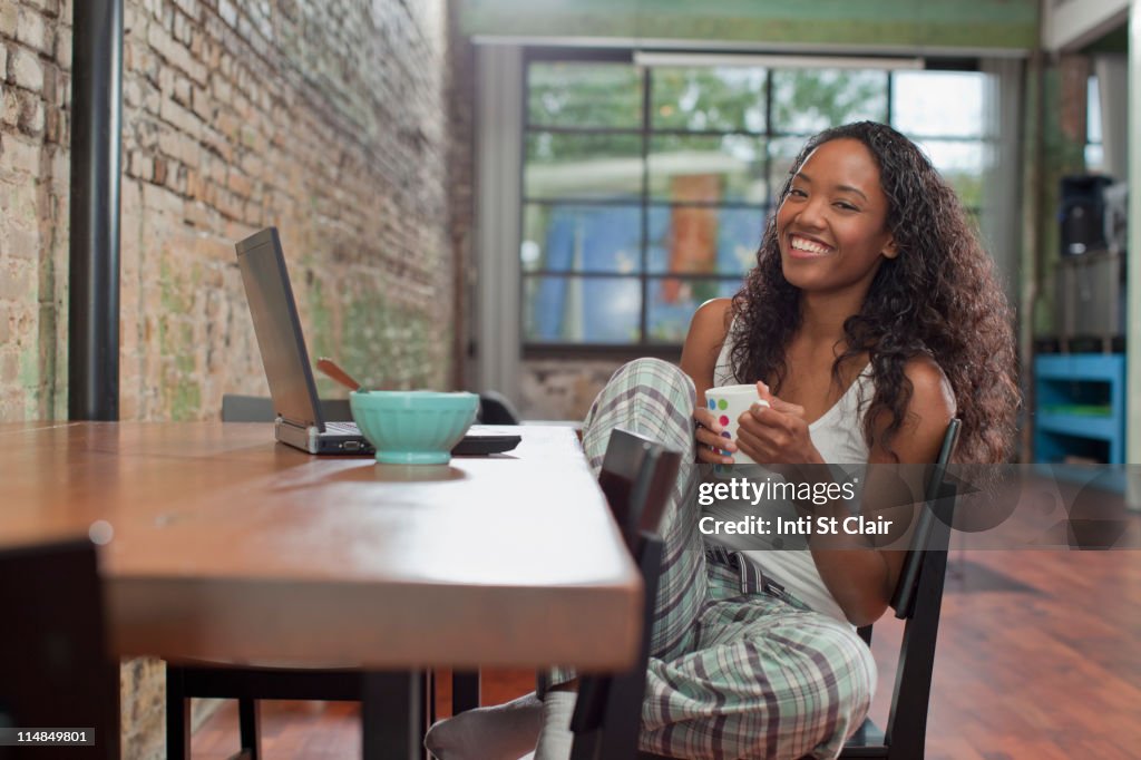 Mixed race woman having breakfast and using laptop
