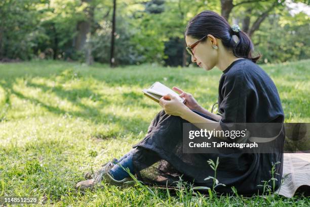 woman reading a book during springtime at the park - mujer leyendo libro en el parque fotografías e imágenes de stock
