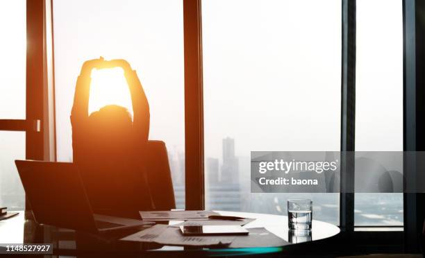 relaxed businesswoman lening back in office - arms raised sunrise stock pictures, royalty-free photos & images