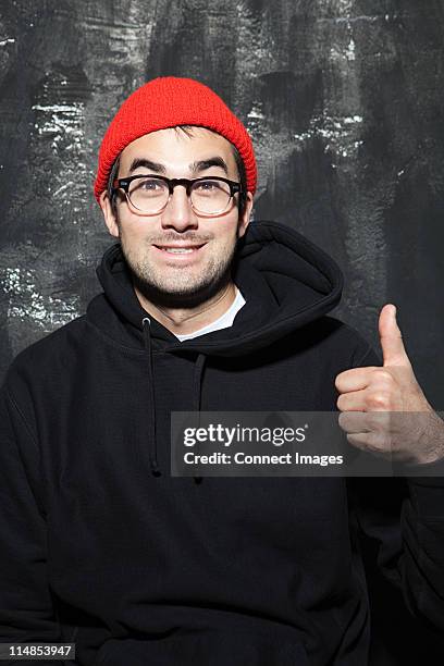 man wearing red knit hat with thumbs up at party - knit hat stockfoto's en -beelden