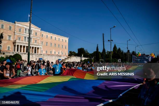 People hold a large rainbow flag as they take part in the Athens Gay Pride in front of the Parliament House in Athens on June 8, 2019. - Thousands...