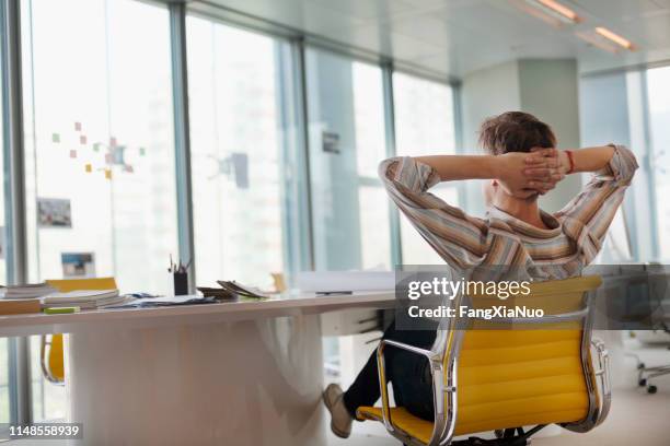 homem que senta-se no escritório do projeto que olha fora do indicador - hands behind head - fotografias e filmes do acervo