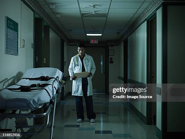 doctor reading medical chart in hospital corridor - working late stockfoto's en -beelden