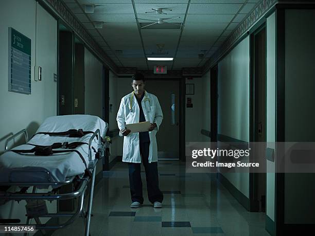 doctor reading medical chart in hospital corridor - working overtime stock pictures, royalty-free photos & images