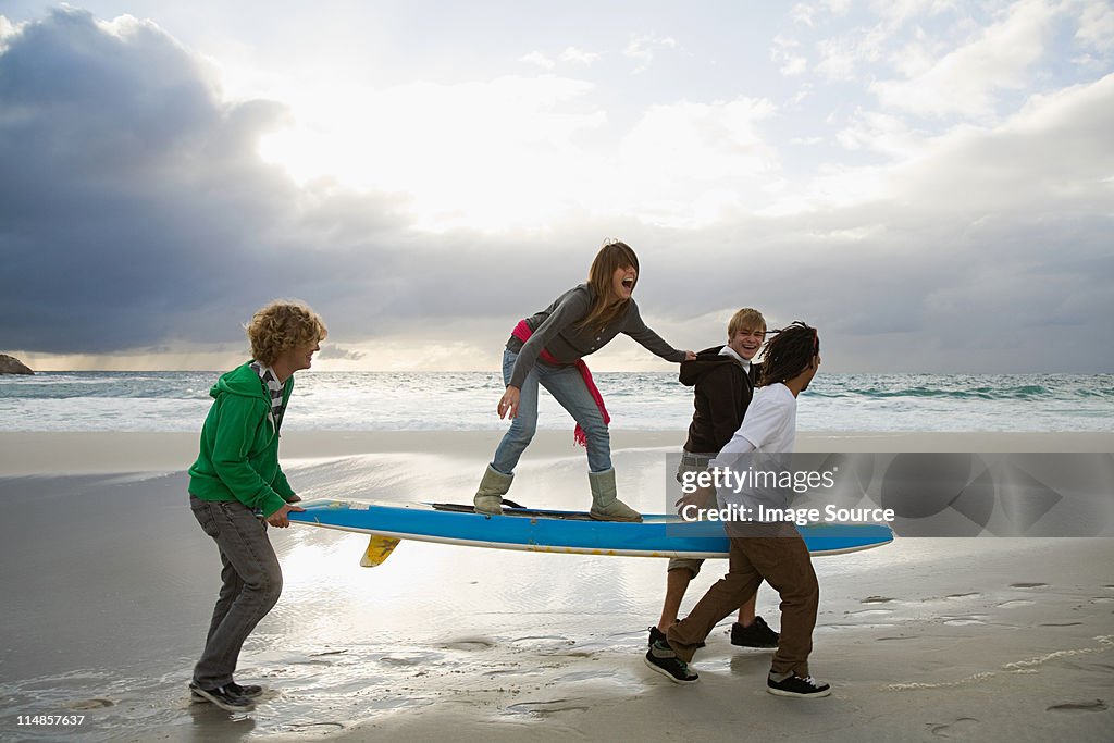 Young people carrying surfboard, person balancing on top