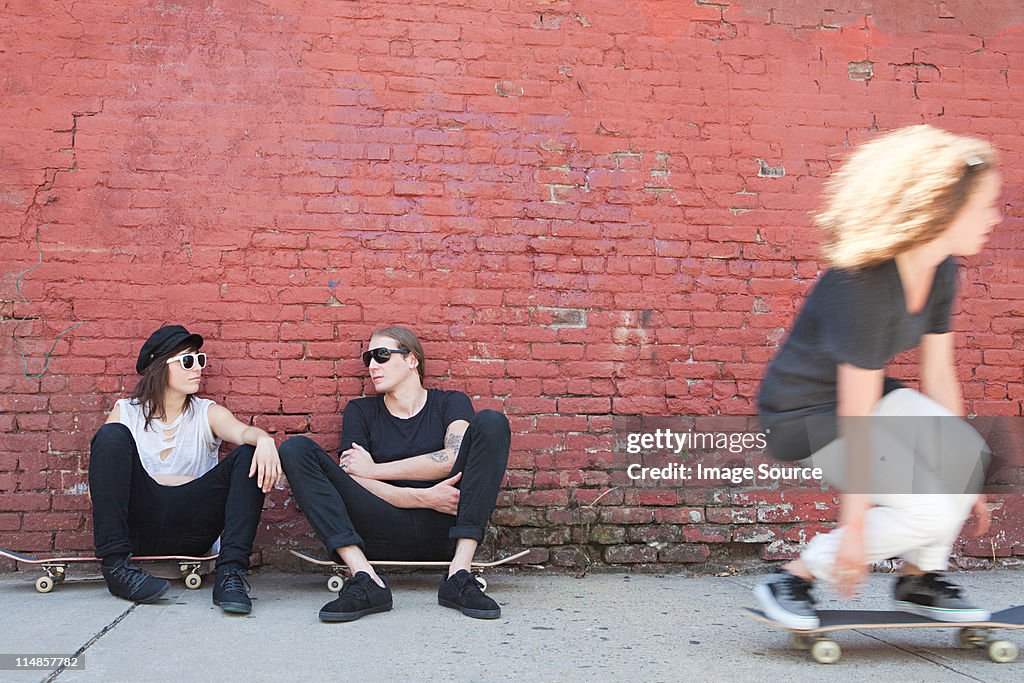Skaters sitting on boards as other skater goes past