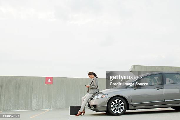 businesswoman texting on mobile phone in car park - parked car no people stock pictures, royalty-free photos & images