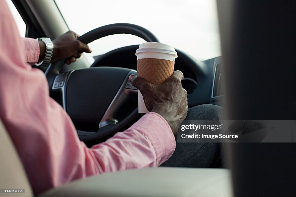 Businessman driving car with disposable cup