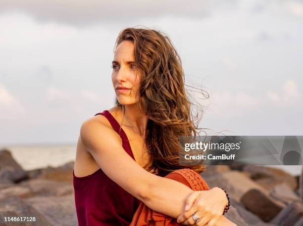 young caucasian bohemian woman by the sea, looks worried. - tousled hair stock pictures, royalty-free photos & images