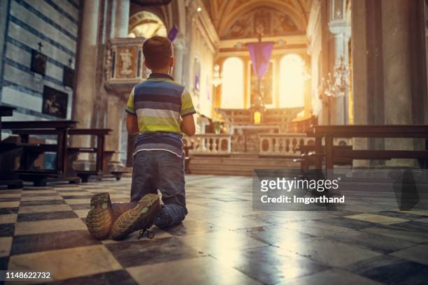 pequeño niño orando en la pequeña iglesia en la pequeña ciudad italiana durante la semana santa - niños orando fotografías e imágenes de stock