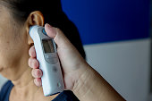 Doctor checking patient's temperature in the ear with Tympanic Thermometer, inside the hospital or clinic.