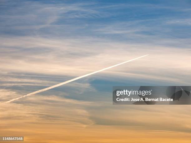 full frame of clouds of colors in sky during sunset with the stele of smoke of a plane crossing the sky. - sunset with jet contrails stock pictures, royalty-free photos & images