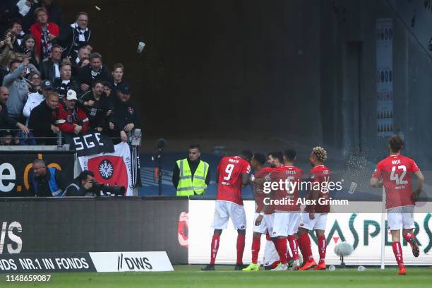 Anthony Ujah of 1. FSV Mainz 05 celebrates with his team mates after scoring his team's first goal as Eintracht Frankfurt supporters throw beers...