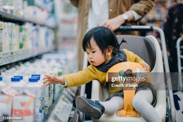 curious little toddler girl grabbing a bottle of fresh milk from the fridge while sitting on shopping cart grocery shopping with mother - woman shopping china photos et images de collection