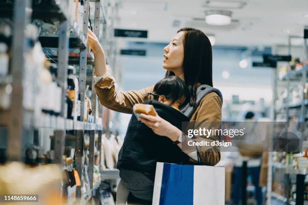 young mother grocery shopping with little daughter in market aisle in a shop - baby bag stock-fotos und bilder