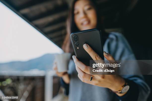 young asian woman using smartphone while relaxing with coffee in the balcony on a fresh morning - phone close up stock pictures, royalty-free photos & images