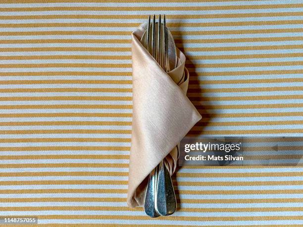 eating utensils rolled in a napkin on striped table - napkin stock pictures, royalty-free photos & images