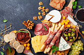 Italian appetizers or antipasto set with gourmet food on kitchen table top view. Mixed delicatessen of cheese and meat snacks with red wine.