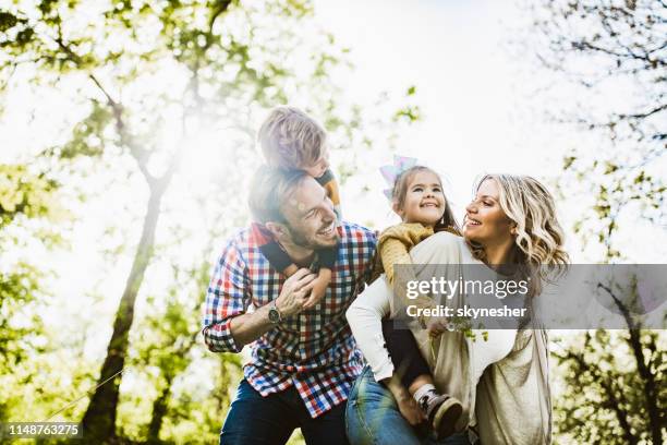 below view of playful family having fun while piggybacking in nature. - springtime family stock pictures, royalty-free photos & images