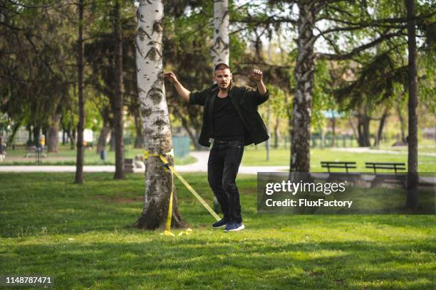 fokussierte junge mann übt seine balancefähigkeiten auf seiner lieblingslackline - slacklining stock-fotos und bilder