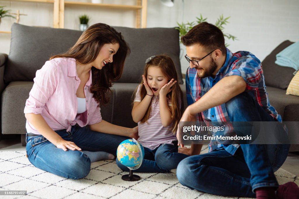 Eltern und Tochter schauen im Wohnzimmer auf den Globus