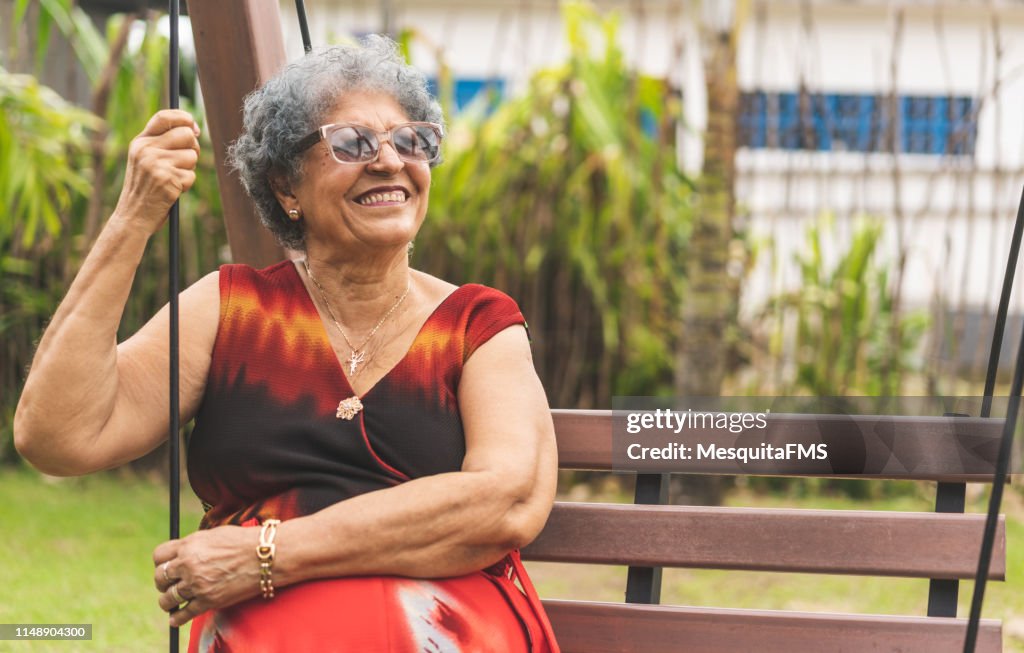 Senior woman relaxing on a wooden swing in public park