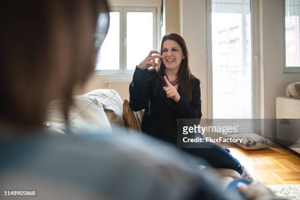 cheerful woman communicating with a friend at home using sign languages - american sign language stock pictures, royalty-free photos & images