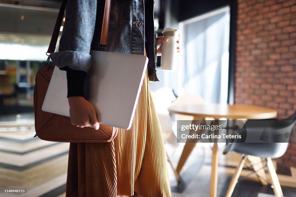 Woman carrying laptop, purse and reusable coffee cup to work