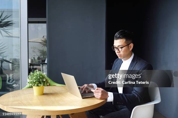 well dressed asian man making an online purchase - asian credit card imagens e fotografias de stock