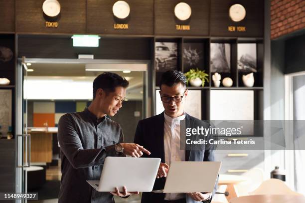 two handsome chinese men standing with laptops in an office - asia stock pictures, royalty-free photos & images