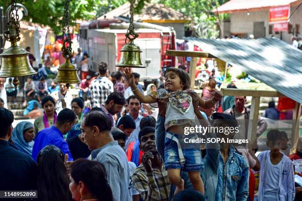 Devotee helps a kid in ringing the bell as a mark of prayers during the annual Hindu festival at the Kheer Bhawani Temple in Ganderbal district,...