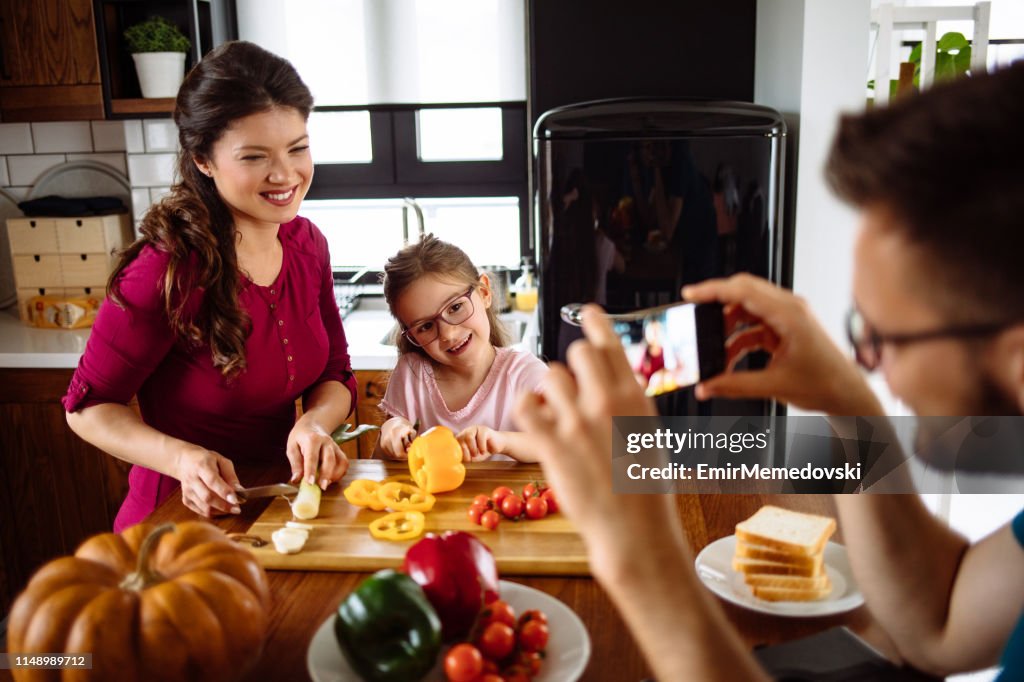 Vater fotografiert Familie am Tisch in der Küche