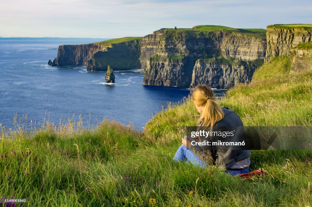 Young woman drawing scenic View Of Cliffs Of Moher, Ireland