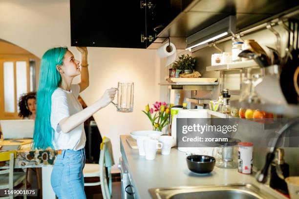 young woman with turquoise hair with coffee can looking for spoon by kitchen sink - cabinet door stock pictures, royalty-free photos & images