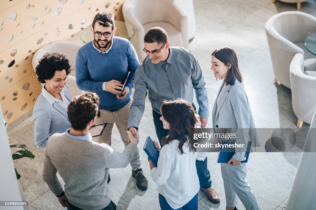 Above view of businessmen shaking hands among their colleagues in a hallway.