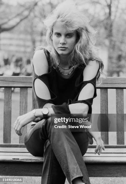 American actress and cellist Lori Singer sitting on a bench in a park, UK, 10th April 1984.