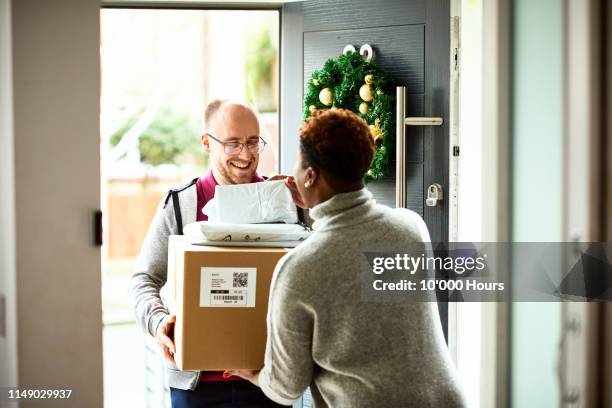 woman checking delivery with cheerful courier at front door - package delivery stock-fotos und bilder