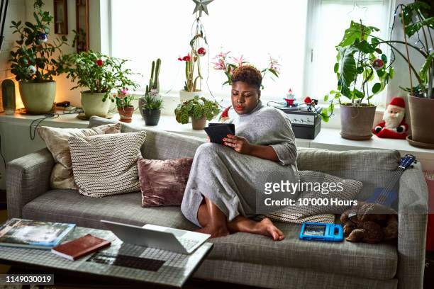 candid portrait of woman relaxing on sofa with digital tablet - e reader stock-fotos und bilder
