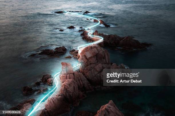 blue light trail following footpath between the stunning coastline during sunrise. - light natural phenomenon stock pictures, royalty-free photos & images