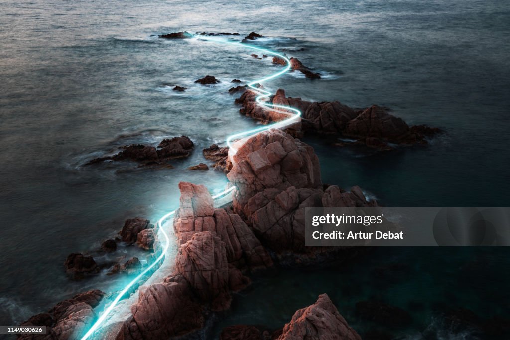 Blue light trail following footpath between the stunning coastline during sunrise.