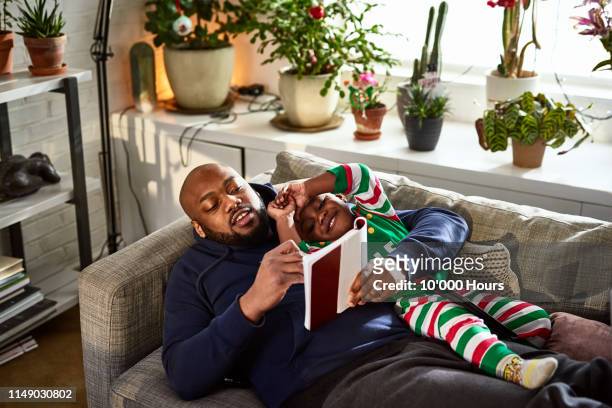 Father lying on sofa with son reading book
