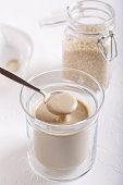 Tahini sauce in glass jar on white background. Natural paste made from sesame seeds.