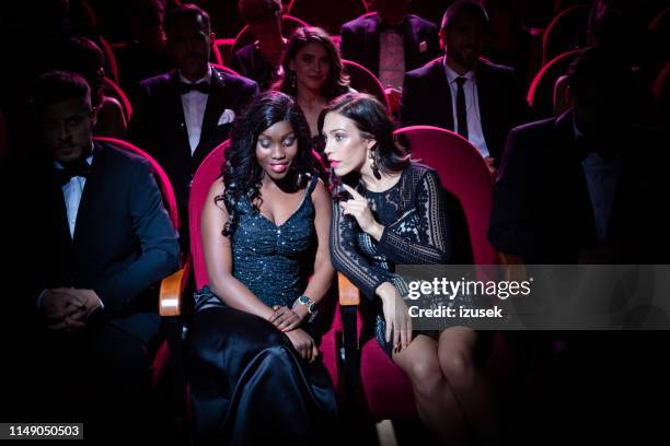 young woman gossiping with friend in opera theater - british film reception inside stock pictures, royalty-free photos & images