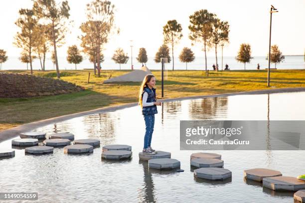 young girl crossing a pond in public park - koper stock pictures, royalty-free photos & images